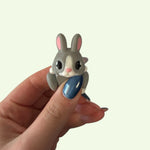 Hand holding a small gray rabbit figurine against a light background