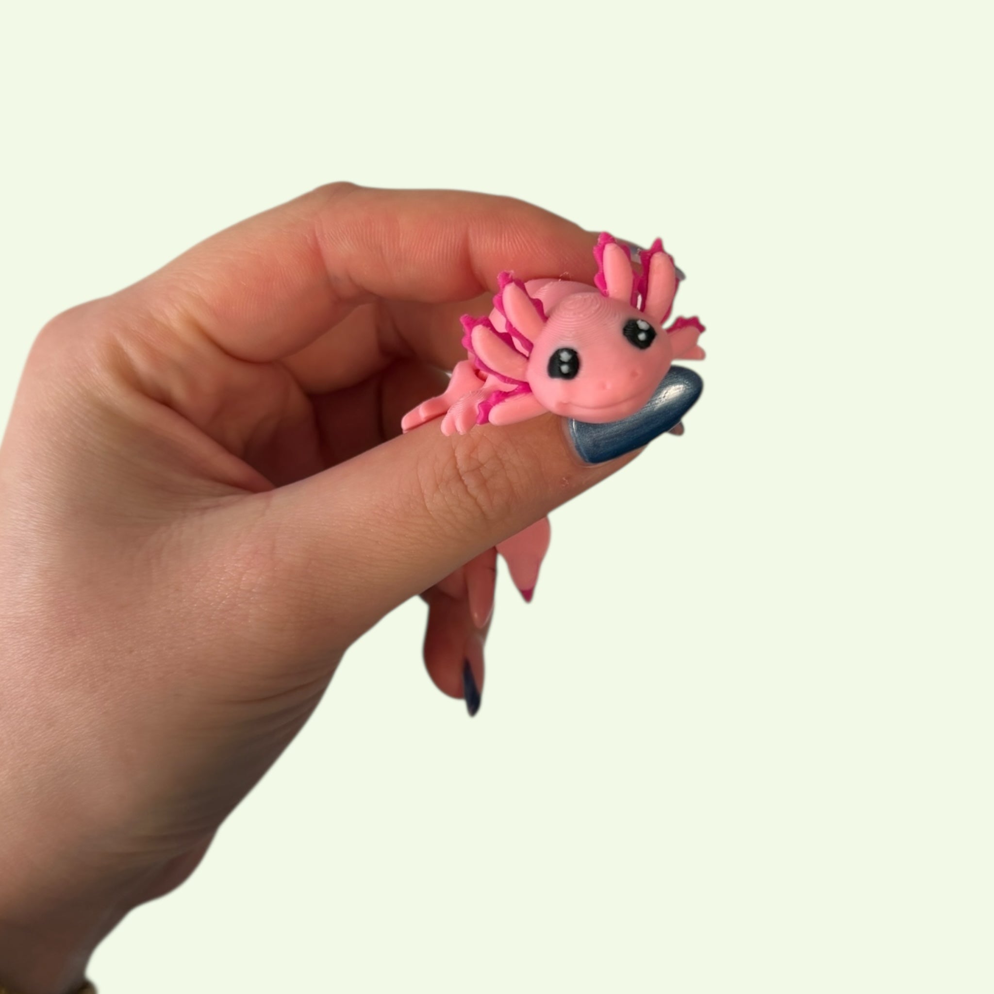 Hand holding a small pink axolotl figurine against a plain background