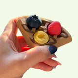 Hand holding a 3D printed waffle clicker with berries on a white background