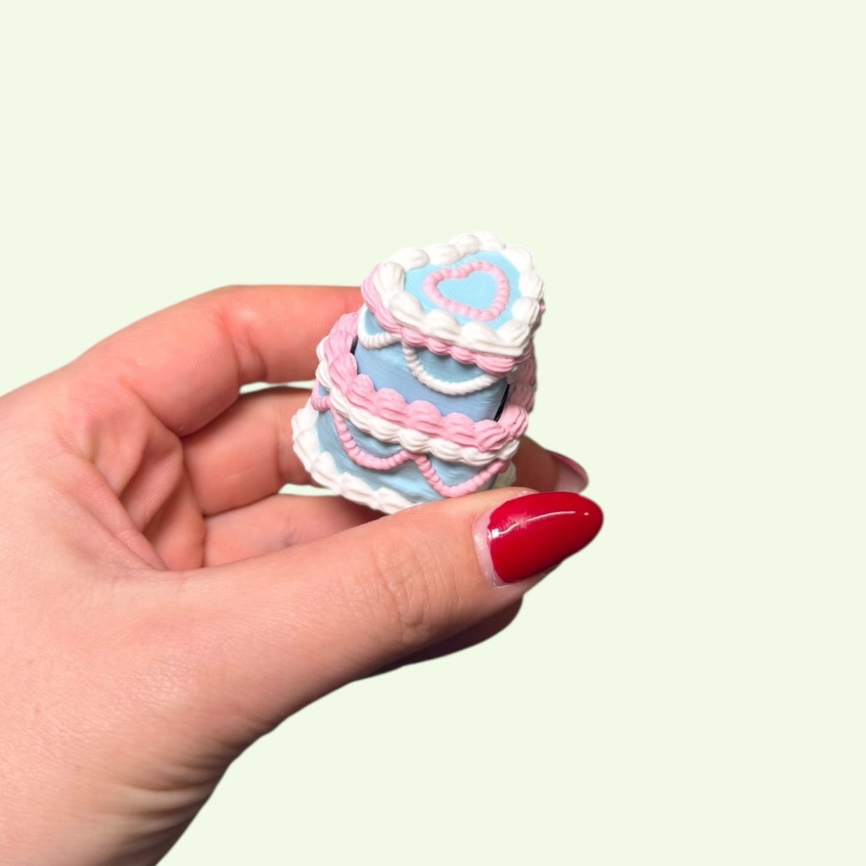 Hand holding a small, colorful cake-shaped object against a light background