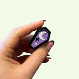 Hand holding a small decorative item with a crescent moon design on a light green background