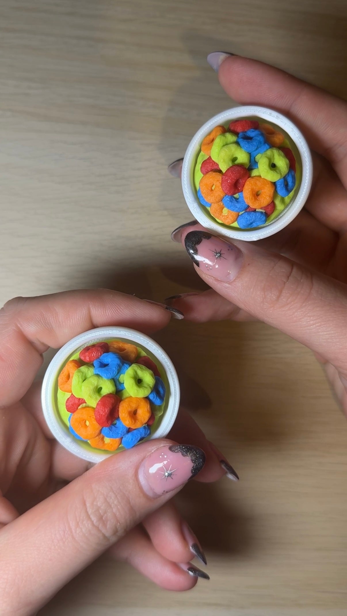 Two small containers filled with colorful cereal loops held by a person's hands on a wooden surface.