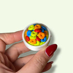 Hand holding a small container with colorful cereal loops on a light background