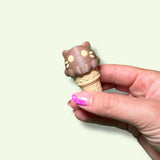 Hand holding a small ice cream cone-shaped toy with a cat design on a light background
