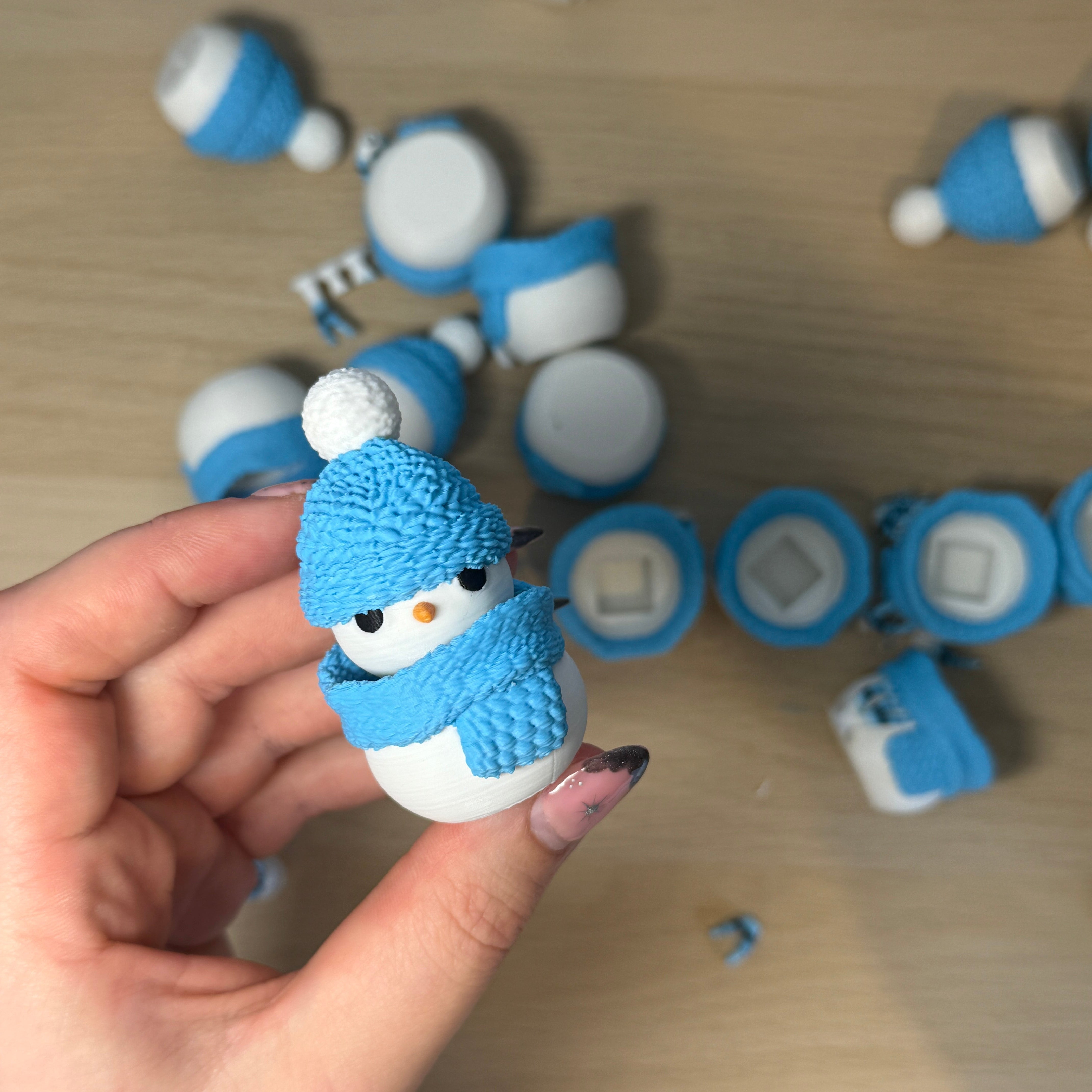 Hand holding a small snowman figurine with more similar figurines on a wooden surface.