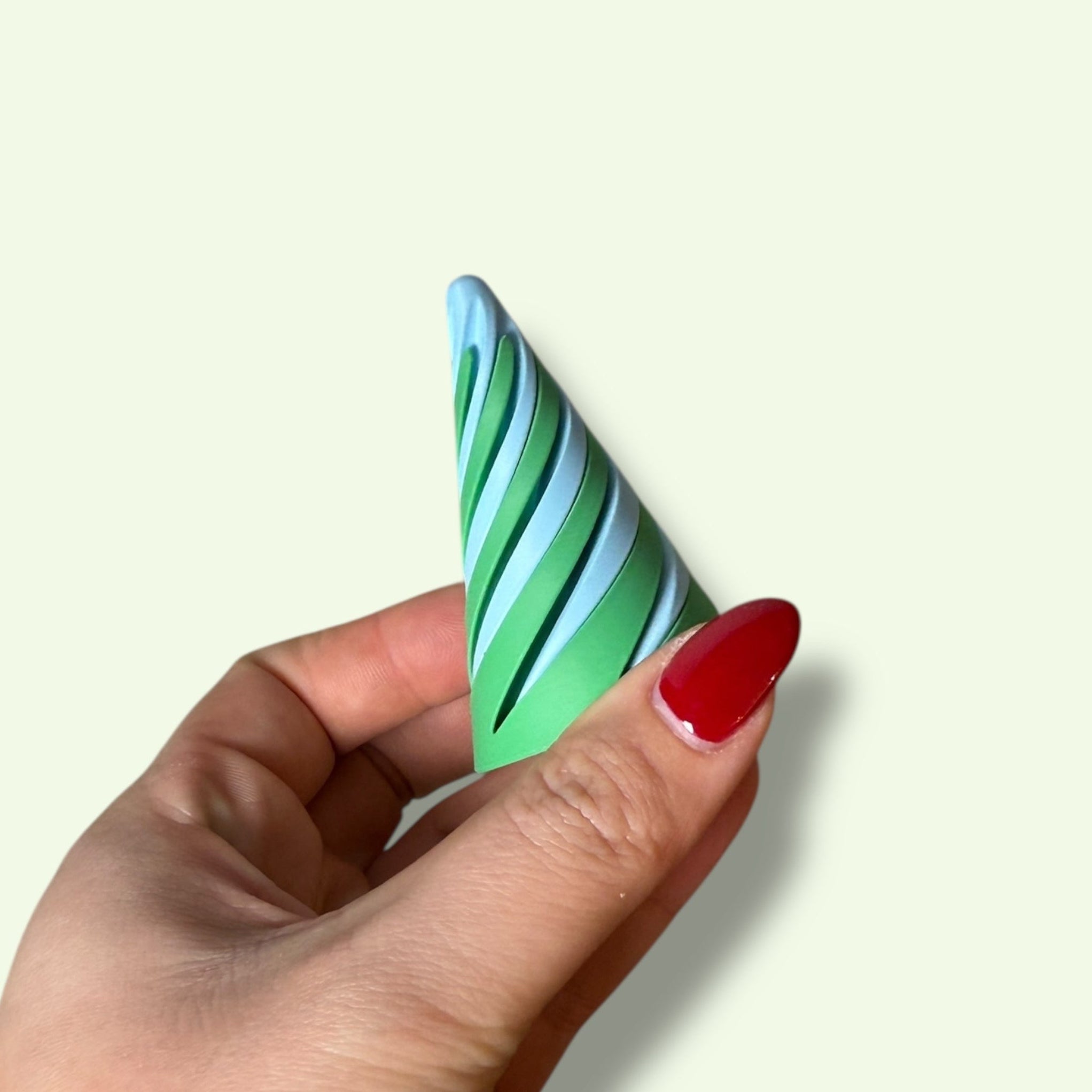 Hand holding a green and white striped cone-shaped object against a light background