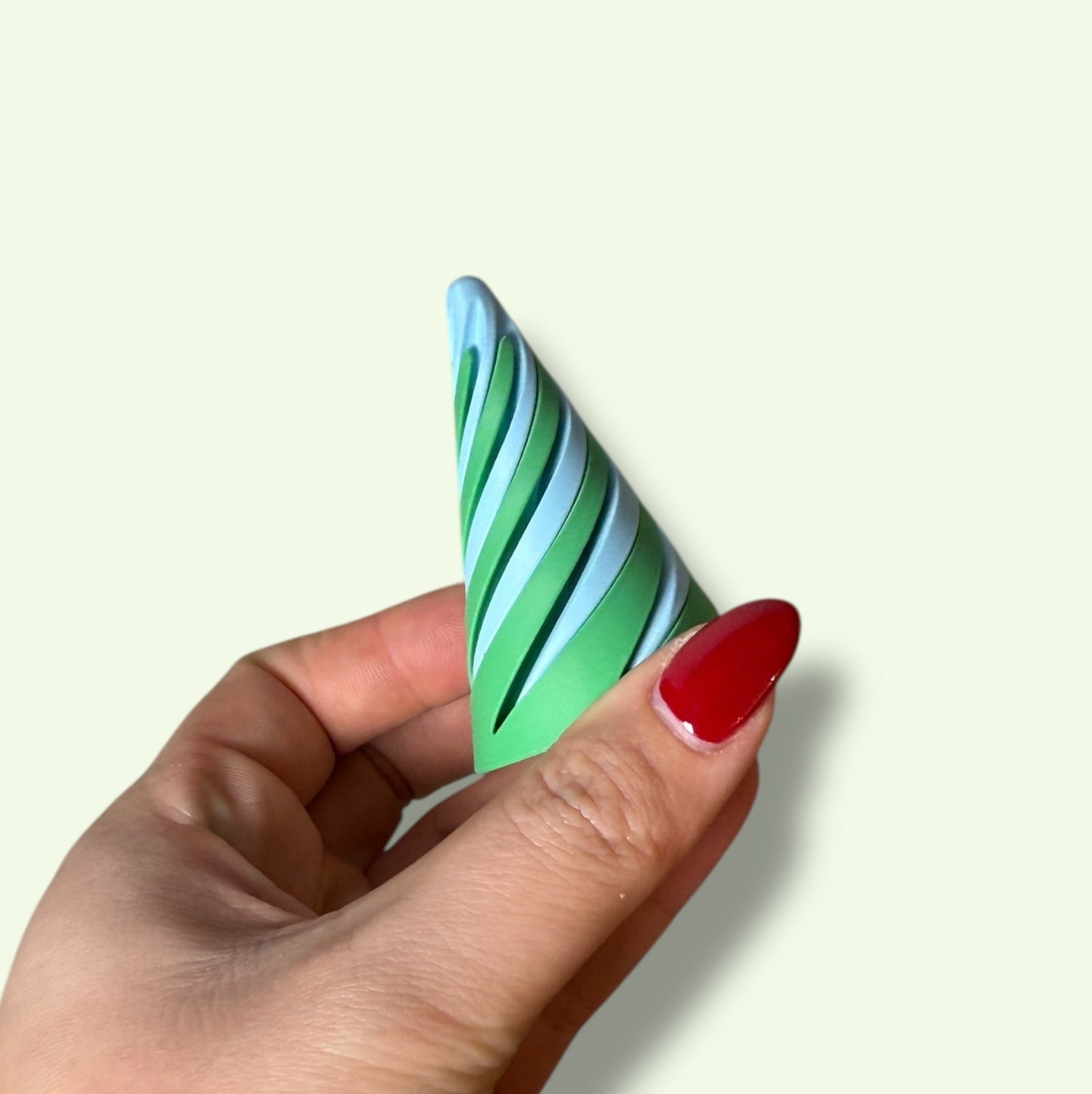 Hand holding a green and white striped cone-shaped object against a light background