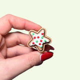 Hand holding a star-shaped cookie with red and green icing on a light beige background