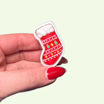 Hand holding a small red and white Christmas stocking charm against a light green background