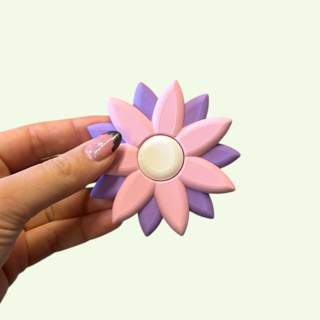 Hand holding a pink and purple flower-shaped object against a light green background