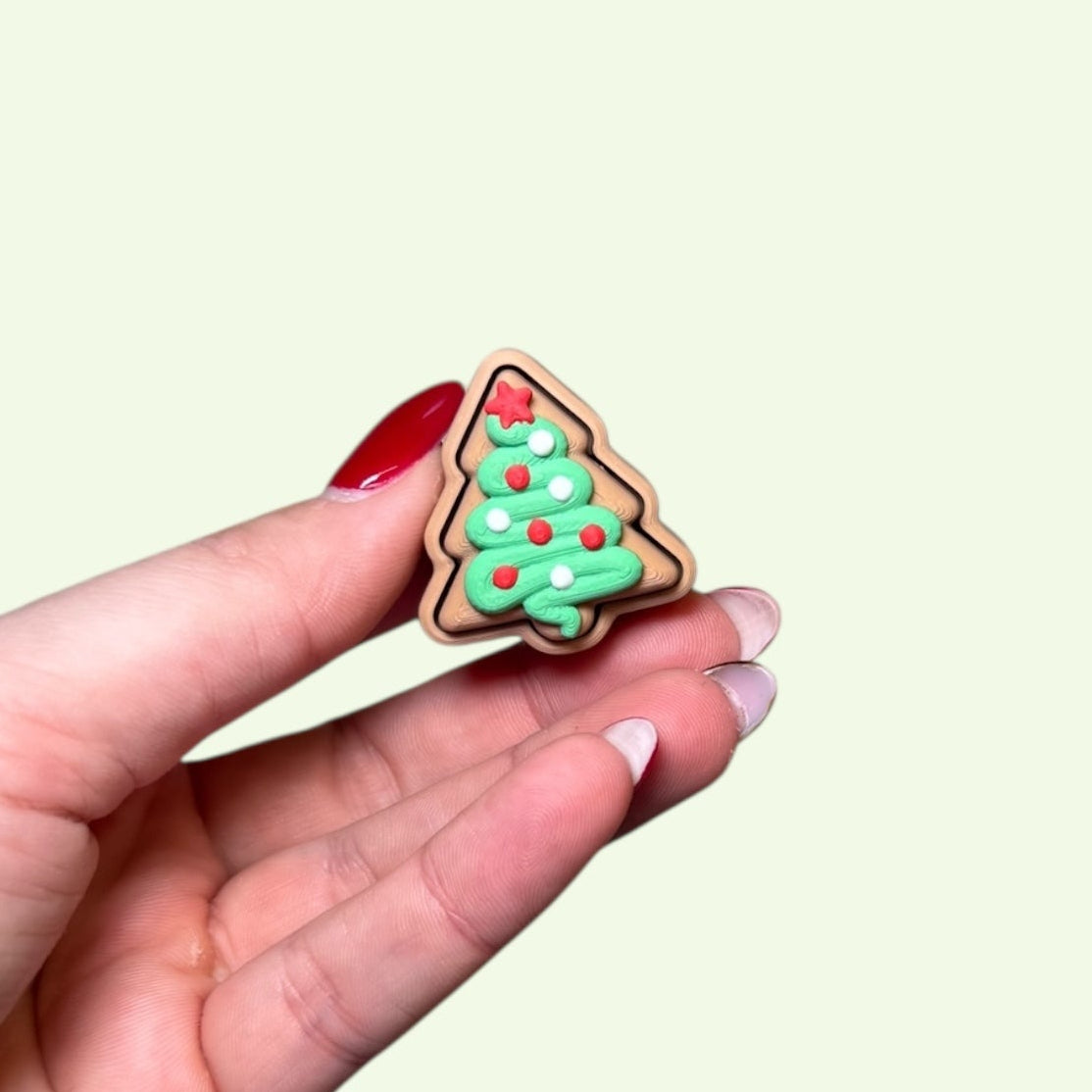 Hand holding a small Christmas tree-shaped cookie against a light background