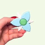 Hand holding a blue and white fidget spinner with a green center against a light green background