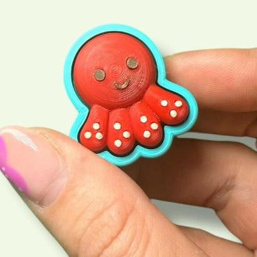 Red octopus charm held between fingers against a white background